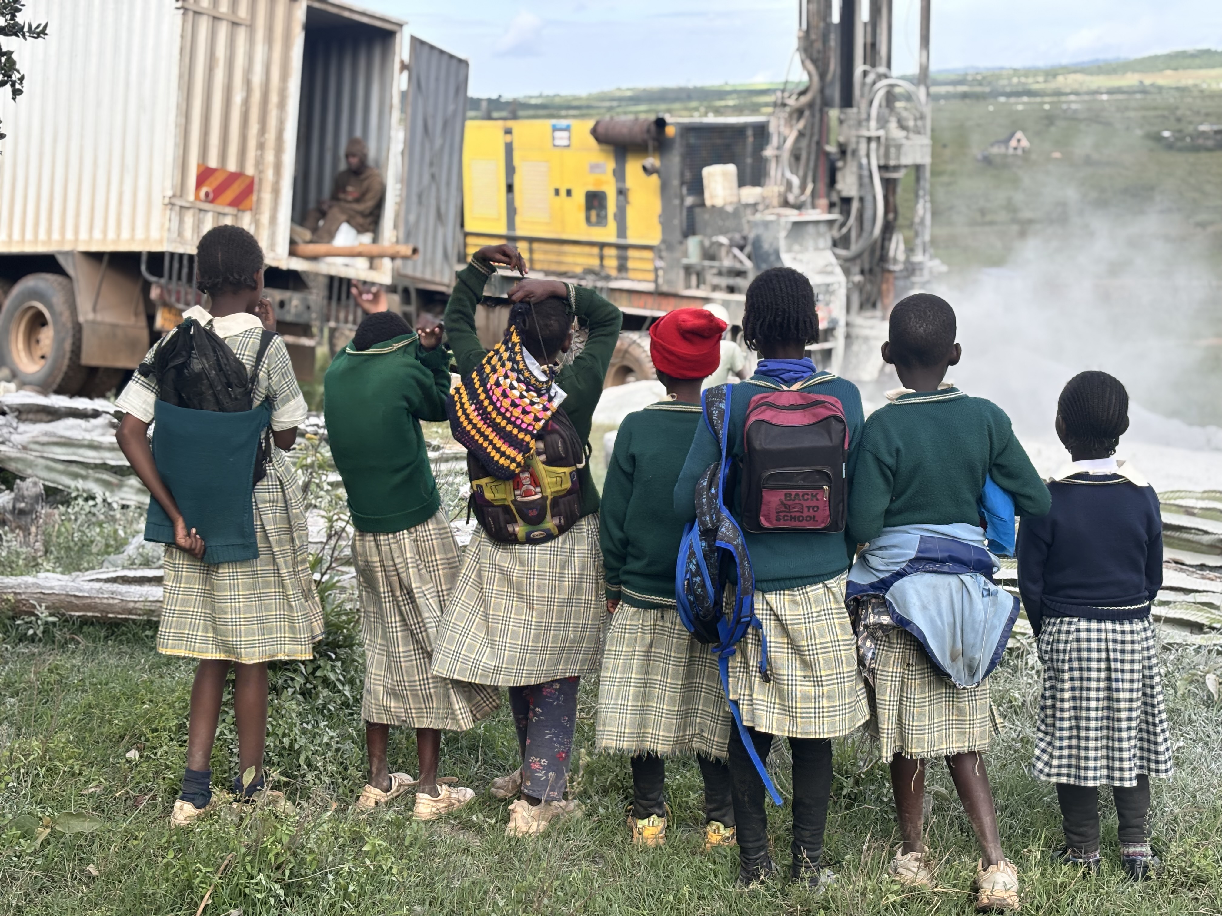 Students in uniform watching borehole drilling Chumvi